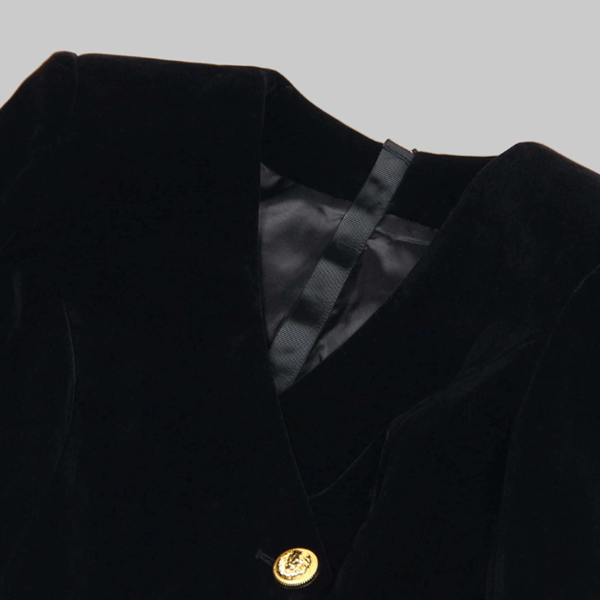 Close-up of a black blazer with a gold button on a white background