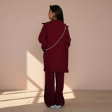 Person wearing a burgundy outfit with a matching coat and pants on a plain background