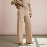Person wearing a beige sweater and wide-leg pants against a pink wall.
