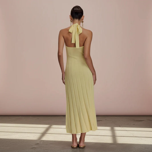 Woman wearing a yellow halter neck dress with a bow detail on a plain background