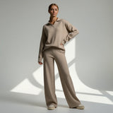Woman wearing a beige sweater and pants standing against a neutral background