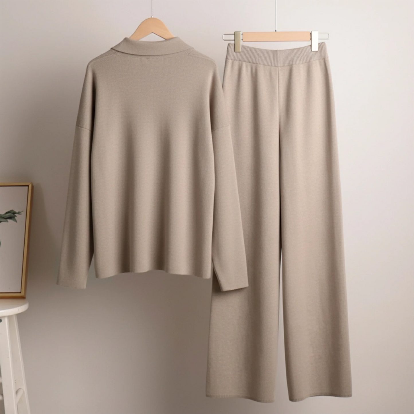 Beige long-sleeve top and wide-leg pants on hangers against a plain wall.