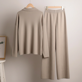 Beige long-sleeve top and wide-leg pants on hangers against a plain wall.