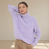 Woman wearing a light purple chunky knit sweater against a plain background