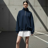 Person wearing a navy blue high-neck sweatshirt on a gray background