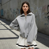 Woman wearing a gray oversized sweater over a white dress with black trim on a light gray background