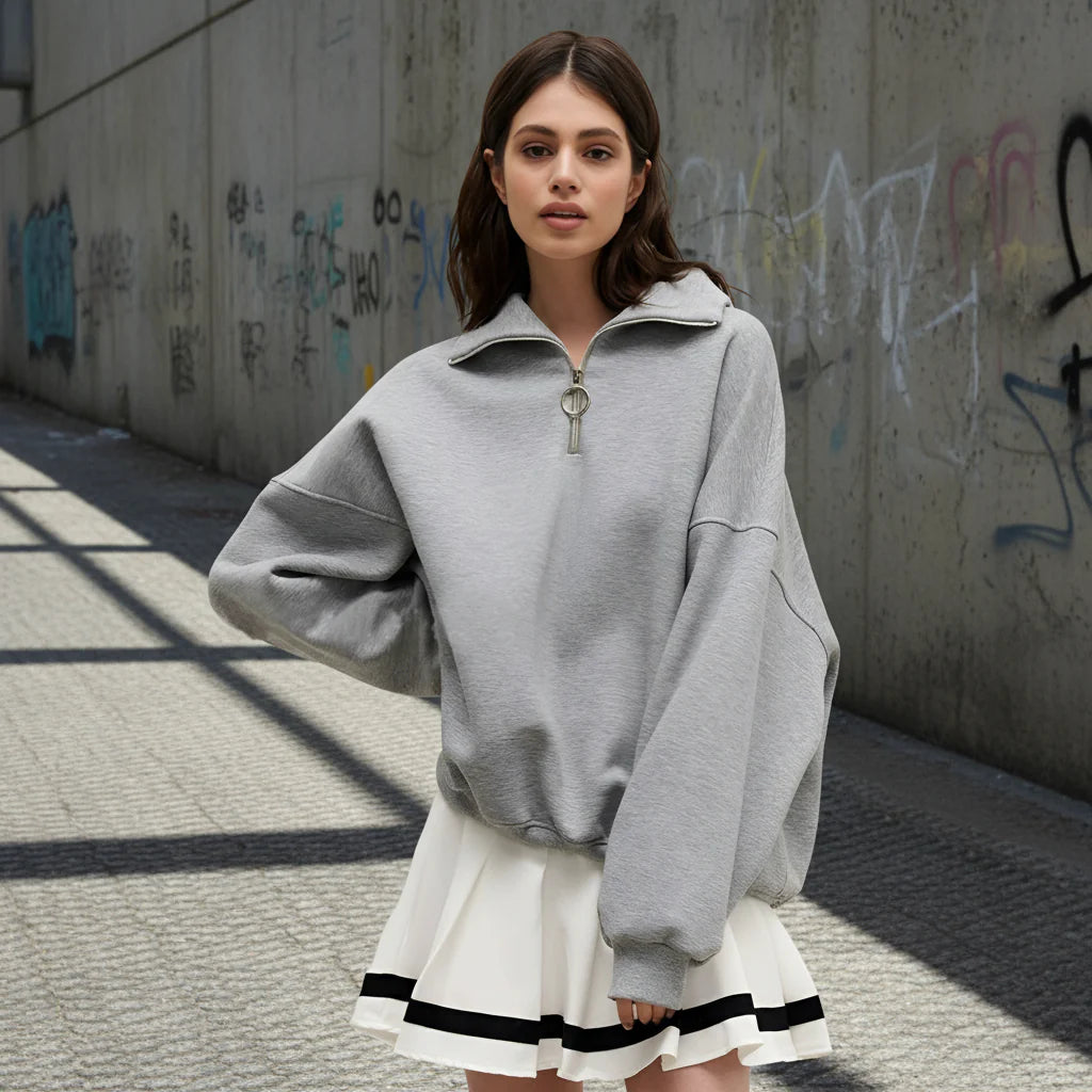 Woman wearing a gray oversized sweater over a white dress with black trim on a light gray background