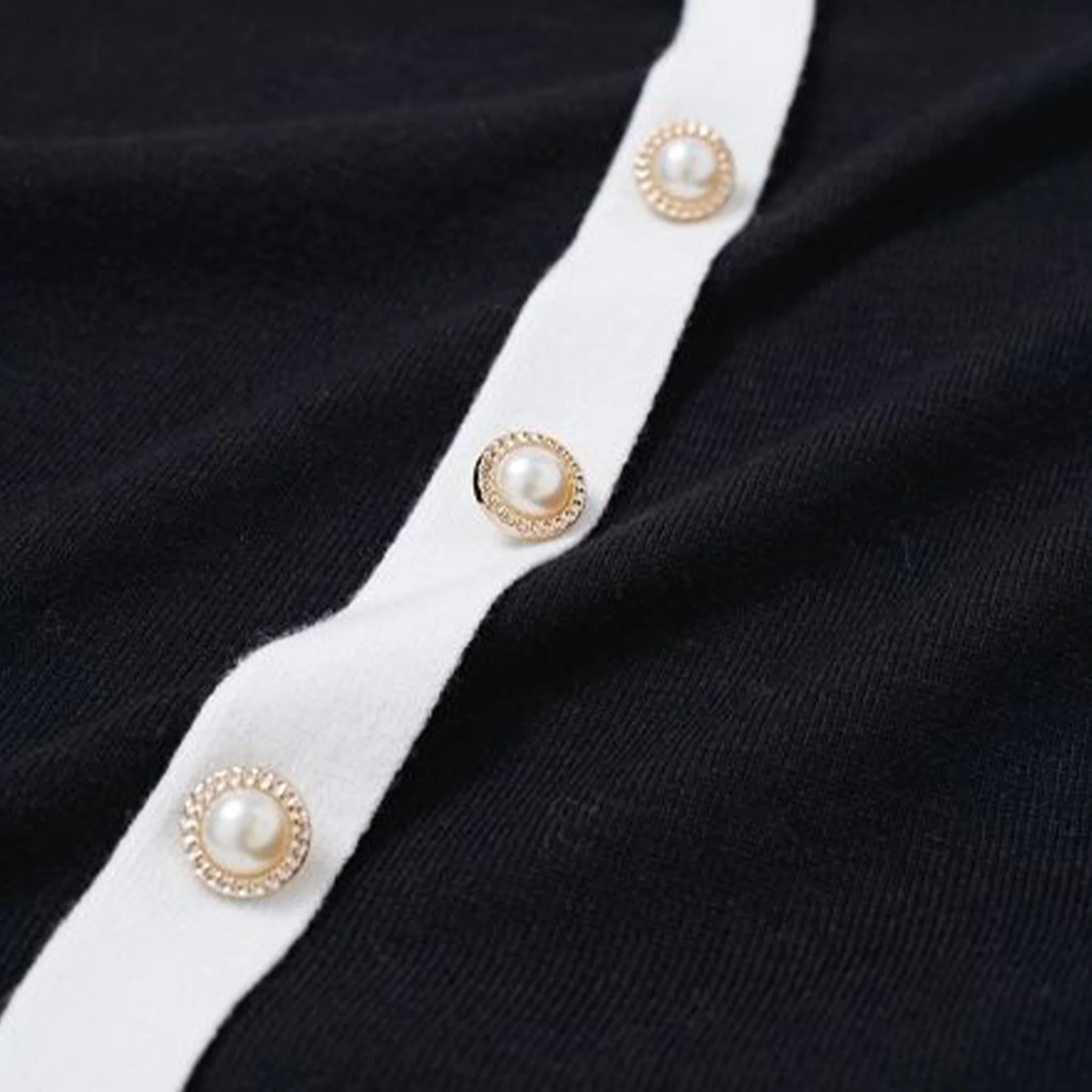Close-up of a black garment with white trim and pearl buttons.