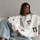 Person wearing a white sweater with black abstract patterns sitting on a couch.