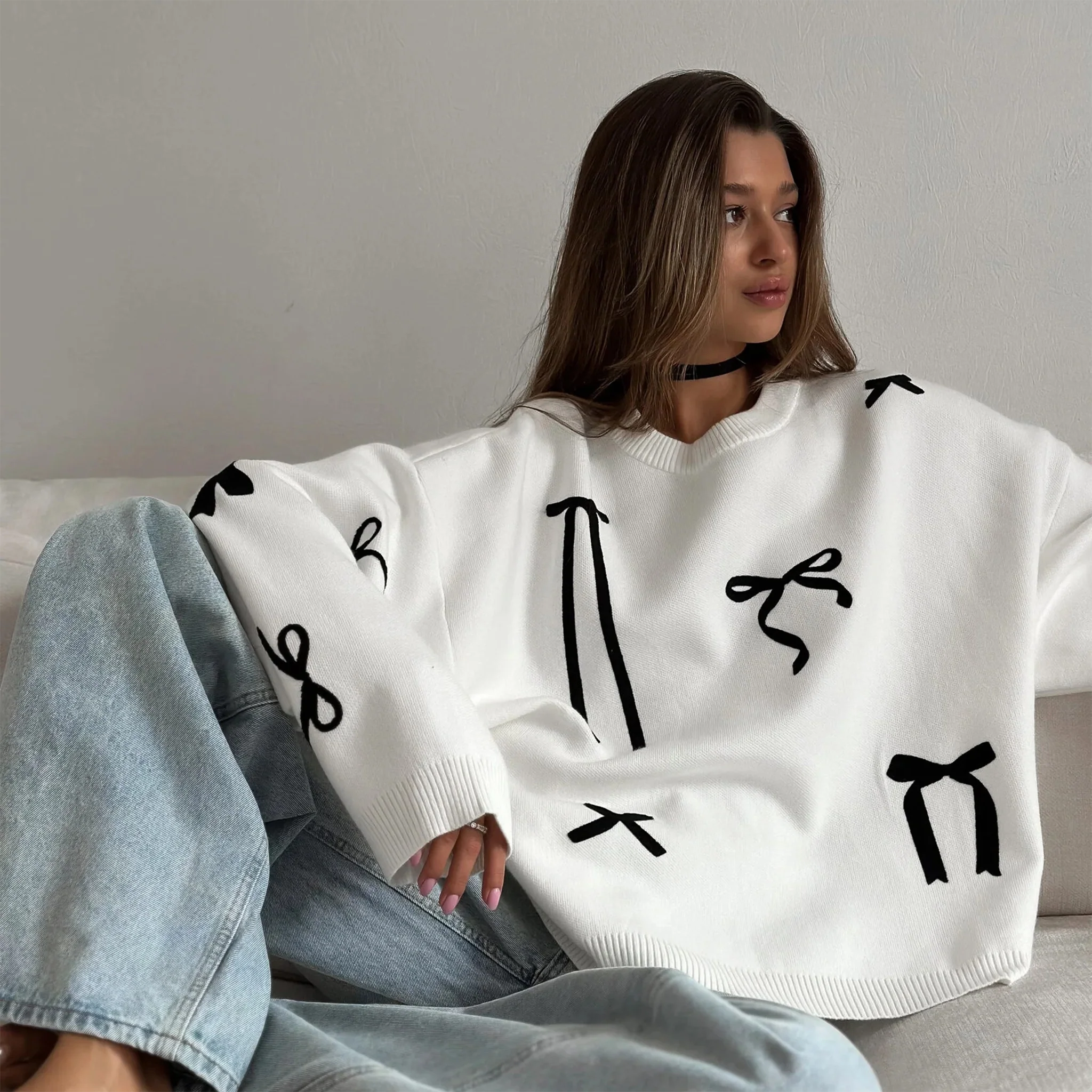Person wearing a white sweater with black abstract patterns sitting on a couch.
