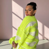 Woman wearing a bright green and white striped sweater against a pink wall.