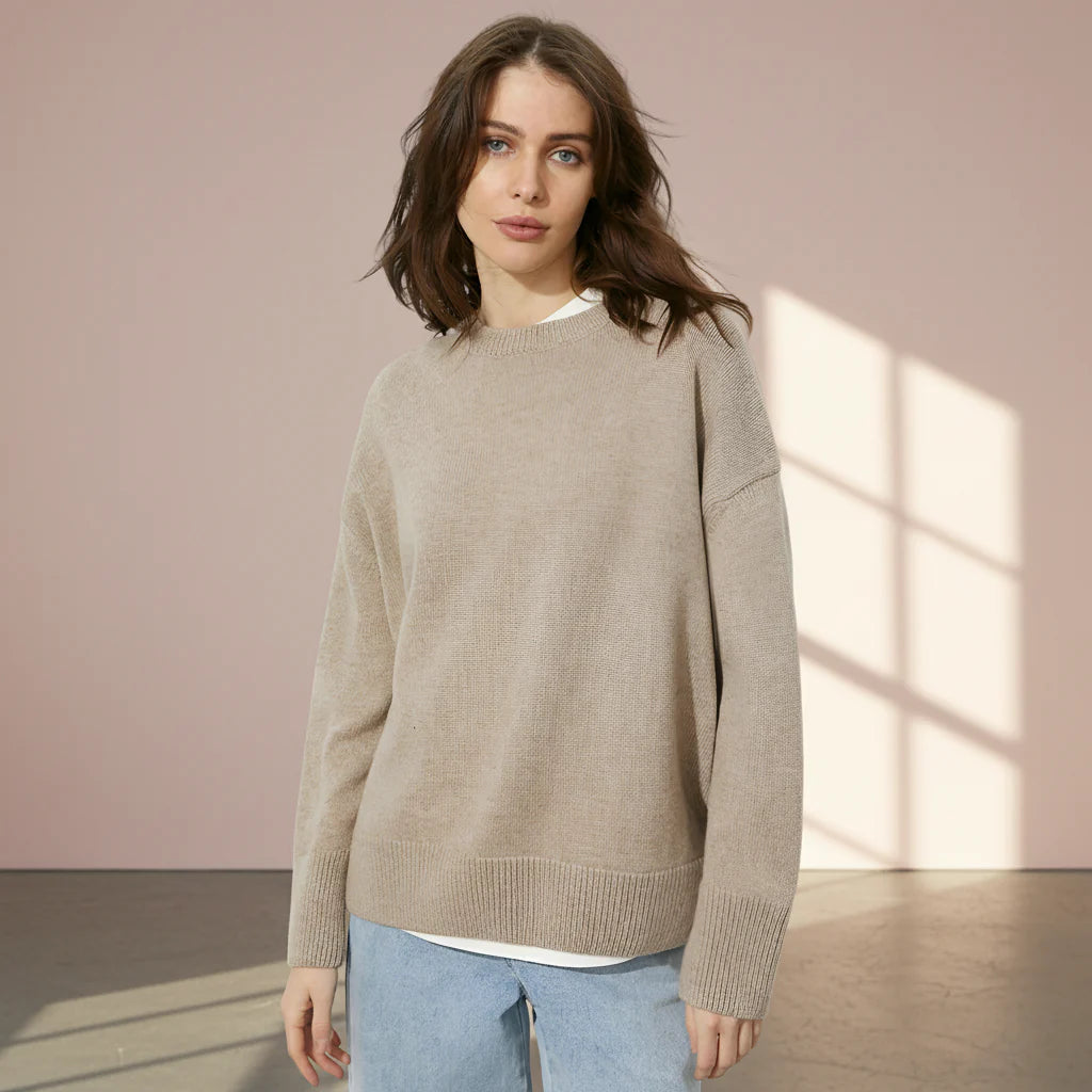 Woman wearing a beige sweater and light blue jeans on a gray background