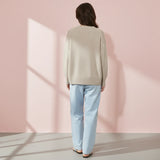 Person wearing a beige sweater and light blue jeans against a pink wall.