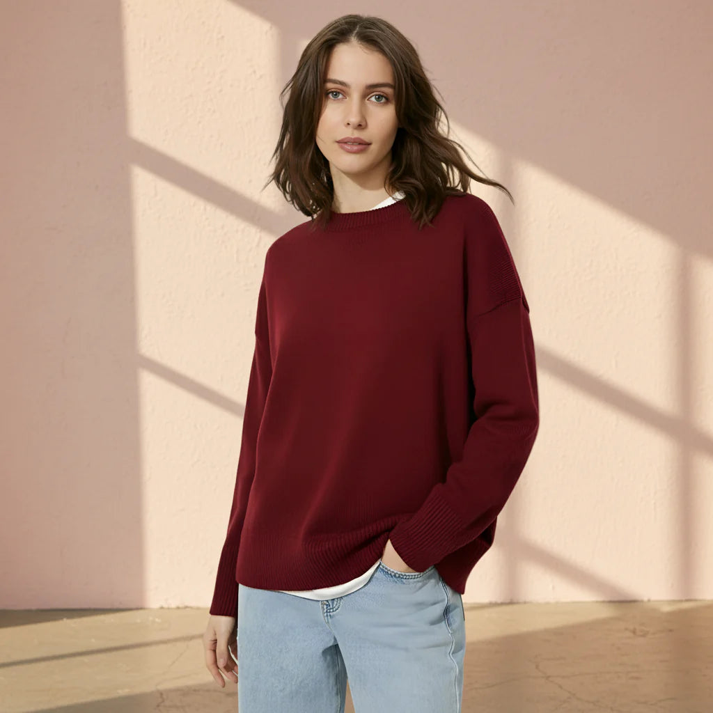Woman wearing a burgundy sweater and light blue jeans on a gray background