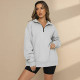 Woman wearing a light gray zip-up sweatshirt and black shorts on a gray background