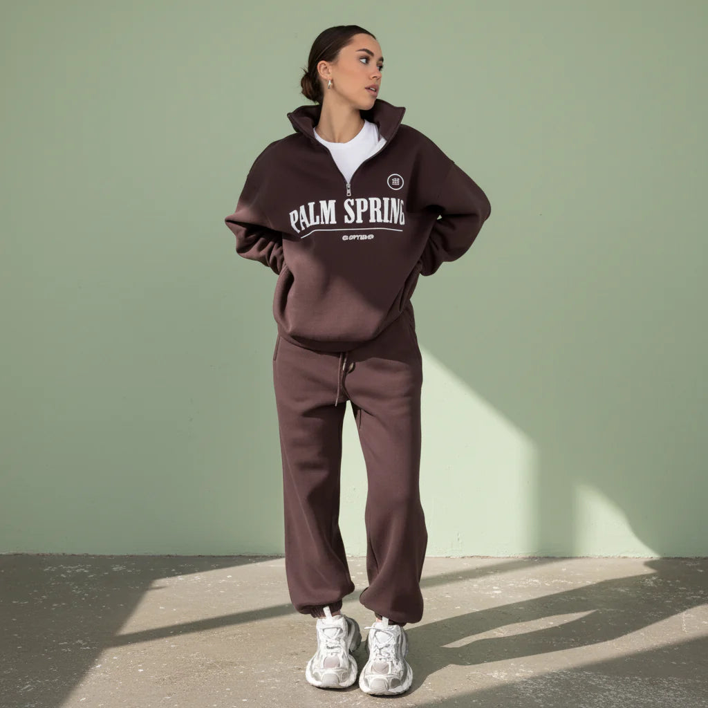 Person wearing a brown 'Palm Springs' tracksuit on a gray background