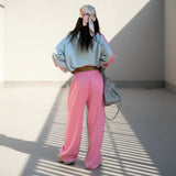 Person wearing a light blue sweatshirt and pink pants with a gray bag on a plain background