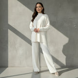 Woman wearing a white outfit standing against a gray wall