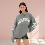 Woman wearing a gray sweater with 'WRESTHER' and number '23' on a plain background